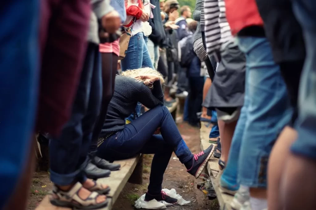 a crown of people standing on benches watching a concert. A single woman is sitting down holding her head