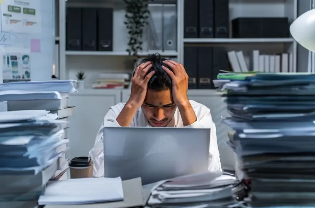 Frustrated man sitting at his desk, holding his head in his hands