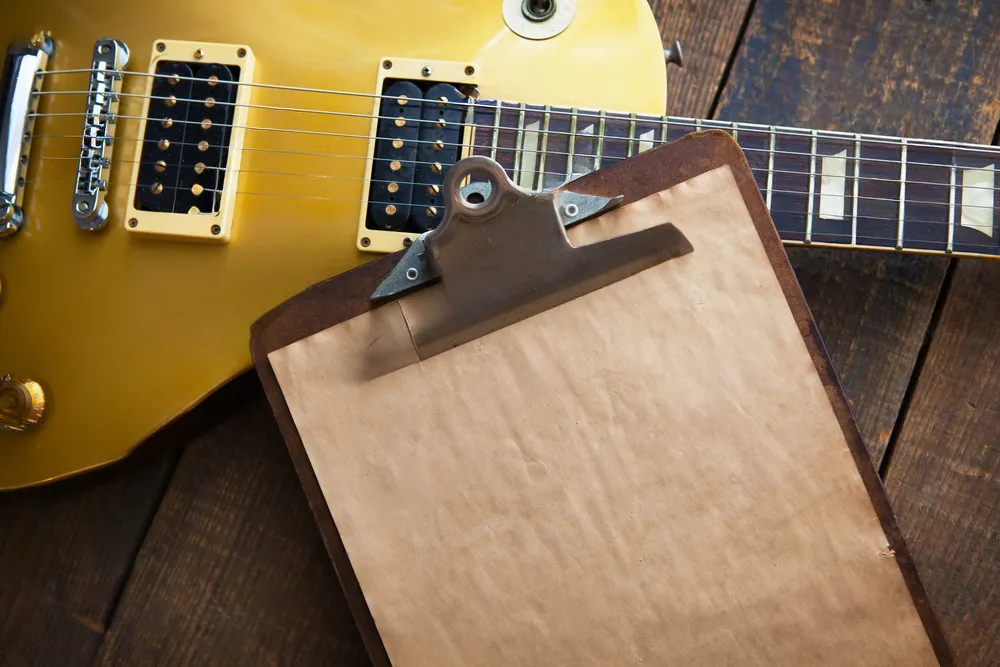 Images of a guitar and a blank clipboard laying on top of it.